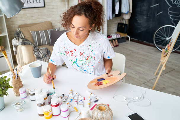 Retrato de mujer joven creativa pintando cuadros con colores al óleo en el escritorio en apartamento moderno
 - Foto, Imagen