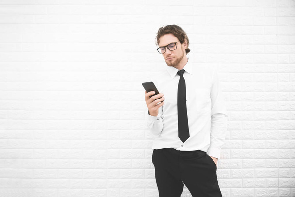 Businessman in formal uniform and using smartphone or mobile phone in front of white wall, Business and fashion concept. Cross processing and Split tone instragram like process. - Fotó, kép
