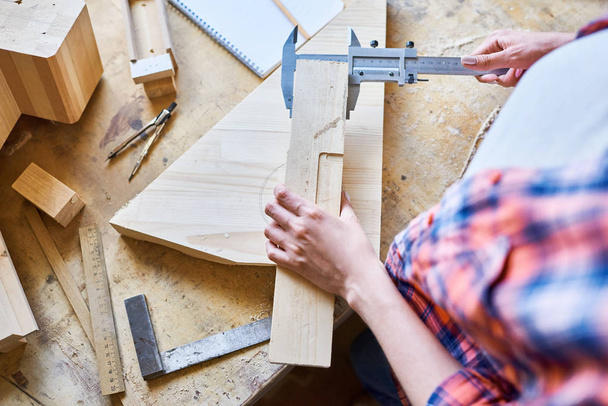 Top view closeup of unrecognizable young woman measuring wooden part making furniture over working table in workshop - Photo, Image