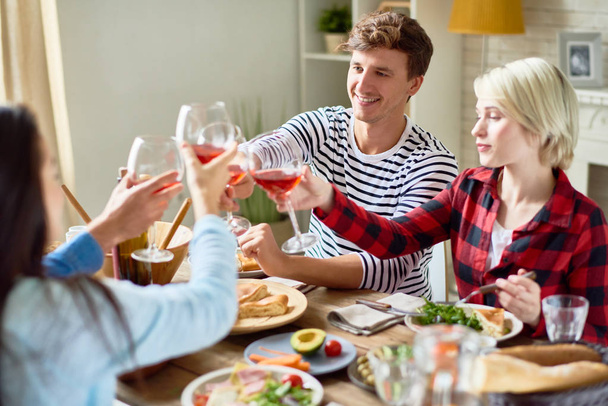 Группа счастливых друзей, наслаждающихся ужином вместе, сидя за большим столом с вкусной едой, звон стаканов в честь праздника
 - Фото, изображение