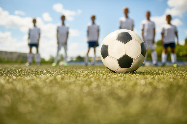Primer plano de la pelota de fútbol en hierba verde con formas borrosas del equipo de fútbol junior en el fondo
 - Foto, imagen