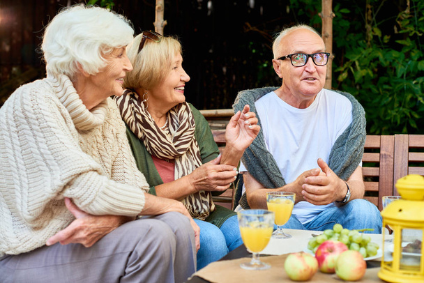 Портрет троих пожилых людей, которые с радостью рассказывают историю встречи за обедом на открытой террасе
 - Фото, изображение