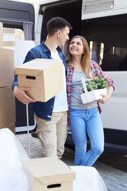 Portrait of happy young couple embracing  while loading cardboard boxes to moving van outside of apartment building - Photo, Image