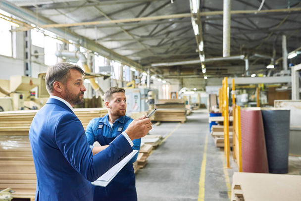 Side view portrait of handsome mature businessman touring modern factory inspecting quality of production, assisted with young workman, copy space - Фото, зображення
