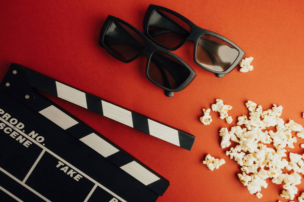Bioscoop minimale concept. Kijken naar de film in de bioscoop. klepel plaat, 3d bril, popcorn op rode achtergrond.  - Foto, afbeelding