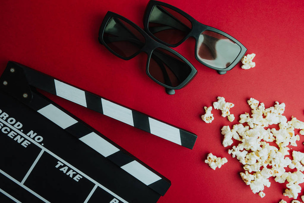 Kino Minimalkonzept. Film im Kino anschauen. Klappbrett, 3D-Brille, Popcorn auf rotem Hintergrund.  - Foto, Bild