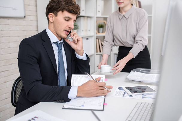 Portrait d'un gestionnaire occupé travaillant au bureau, parlant par téléphone, prenant des notes et utilisant un ordinateur
 - Photo, image