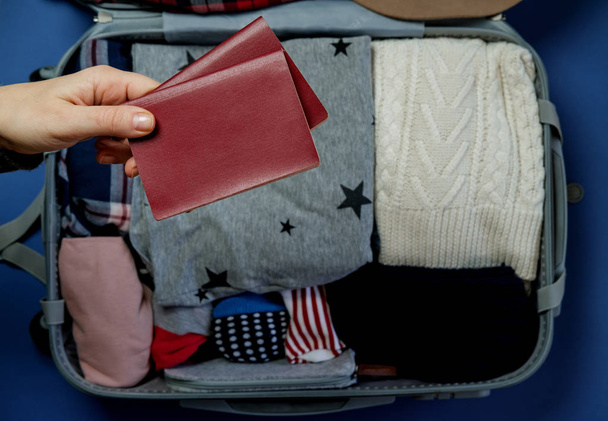 Woman hands with passports on the background Open suitcase packed for travelling. Winter vacations and holidays. Top view - Photo, Image