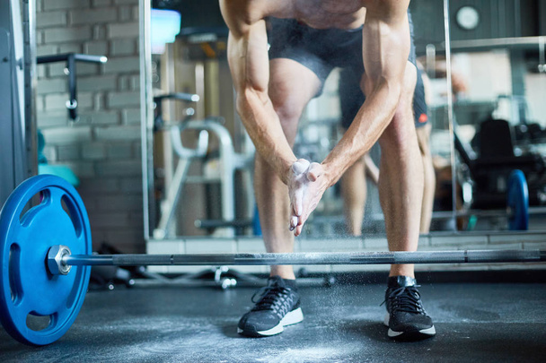 Retrato de sección baja de un hombre musculoso irreconocible listo para levantar pesadas pesas mientras hace ejercicio en el gimnasio moderno
 - Foto, imagen