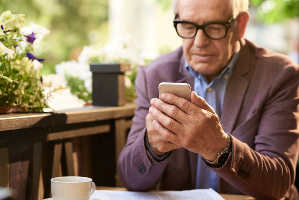 Портрет сучасного старшого чоловіка, який використовує смартфон у відкритому кафе, набирає текстові повідомлення
 - Фото, зображення