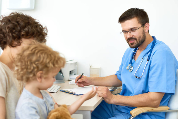 Porträt eines lächelnden Arztes im Gespräch mit einem kleinen Jungen bei einem Termin - Foto, Bild