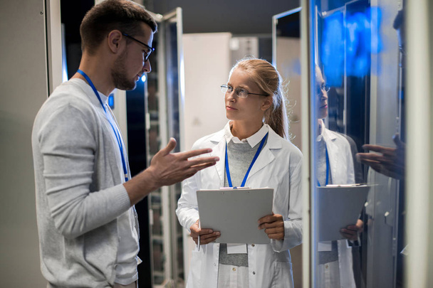 Retrato de dois cientistas, homem e mulher, em pé junto aos gabinetes de servidores e discutindo dados enquanto trabalhava com supercomputador no centro de pesquisa
 - Foto, Imagem