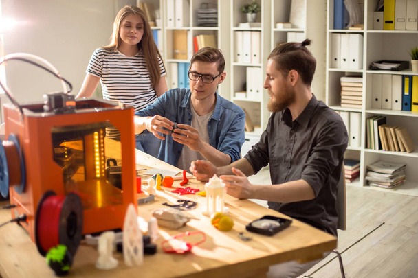 Portrait of three young people using 3D printer working on creative design project together studying in college - Photo, Image