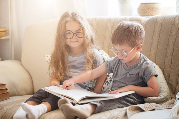 Little brother and sister reading a book on the sofa - 写真・画像