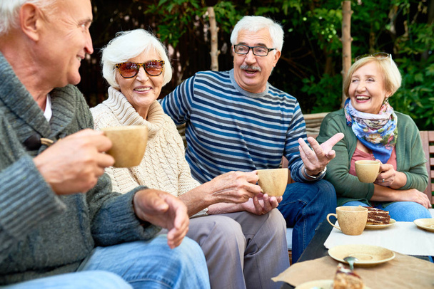 Vrolijke groep senior vrienden genieten van elkaars bedrijf terwijl het hebben van thee partij op de prachtige patio, ze dragen van gebreide truien - Foto, afbeelding