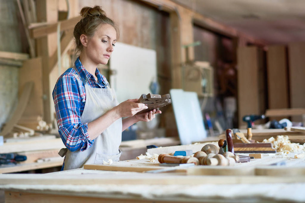 Retrato de una joven carpintera mirando partes de madera en un taller moderno, espacio para copiar
 - Foto, Imagen