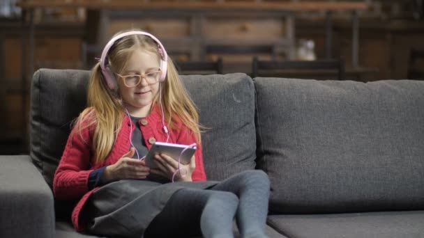 Cute girl in headphones using touchpad on sofa - Metraje, vídeo