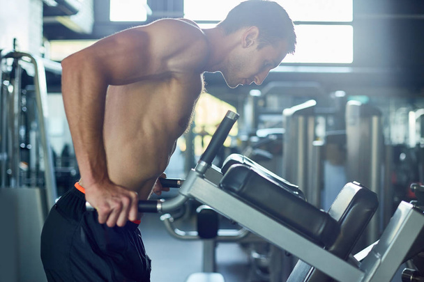 Retrato de vista lateral motivacional de un hombre musculoso guapo con pecho desnudo haciendo ejercicio en un club deportivo
 - Foto, imagen