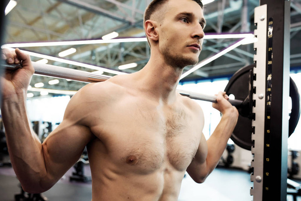 Retrato del hombre fuerte y desnudo que bombea los músculos de los brazos haciendo ejercicio con pesadas barras durante el entrenamiento en el gimnasio moderno
 - Foto, imagen