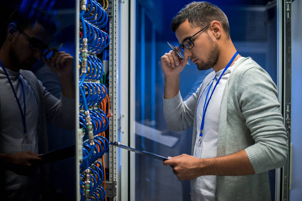 Boční pohled portrét mladého muže stojící serverem kabinet při práci s superpočítač v datovém centru a hospodářství schránky - Fotografie, Obrázek