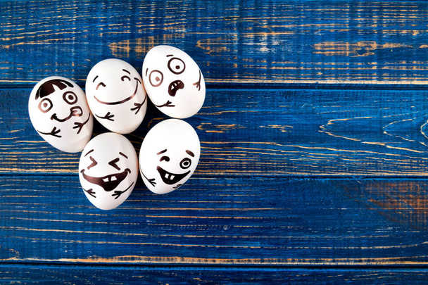 Funny easter eggs with different funny faces on blue wooden background. Top view. - Photo, Image