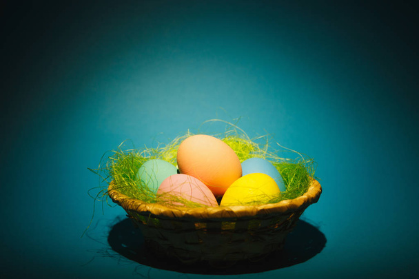Colorato pastello monofonico tradizionale dipinto uova di Pasqua in cesto con erba verde su sfondo blu scuro con ombre nere, silhouette, luce. Copia spazio per pubblicità. Con posto per il testo
 - Foto, immagini