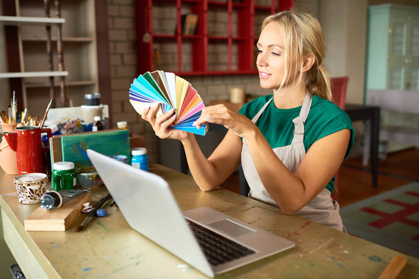 Portrait d'artiste blonde féminine regardant des échantillons de couleurs choisir la palette pour le projet d'art et d'artisanat en atelier
 - Photo, image