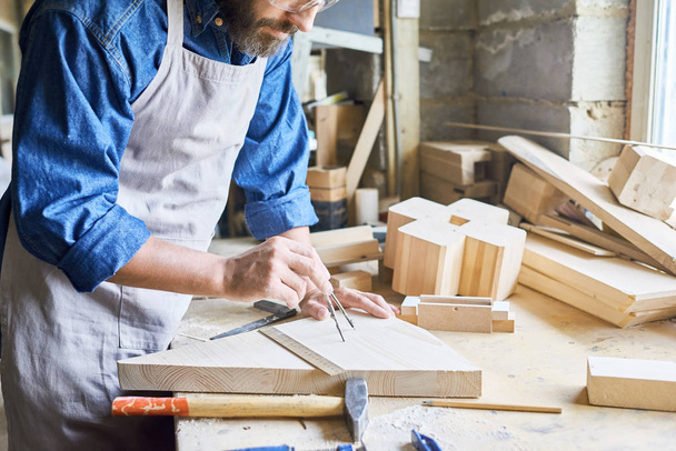 Portrait rapproché de solides mains masculines marquant un morceau de bois avec instrument de mesure dans un atelier de menuiserie fabriquant des meubles
 - Photo, image