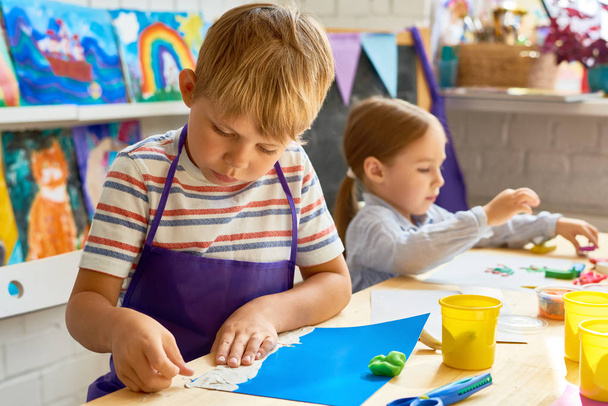 前の学校のアートとクラフトのクラスで粘土画像を作るエプロンを着ているかわいい男の子の肖像画 - 写真・画像