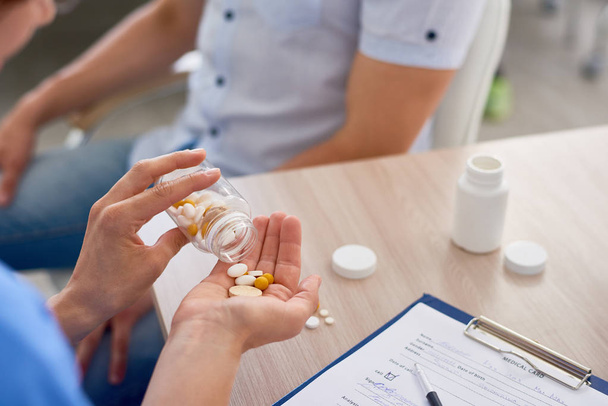 Крупним планом молода жінка-лікар дає таблетки і вітаміни пацієнту в офісі
 - Фото, зображення