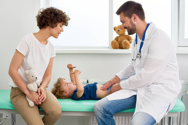 Портрет усміхненого лікаря, який вивчає шлунок маленького хлопчика і просить його сказати, де болить
 - Фото, зображення