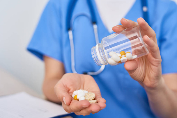 Close-up shot van onherkenbaar arts dragen blauwe uniform gieten pillen uit de fles - Foto, afbeelding