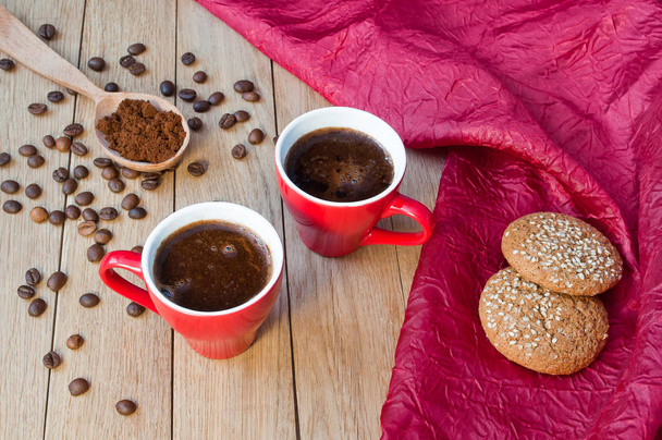 Две красные чашки кофе с овсяным печеньем на деревянном столе
 - Фото, изображение