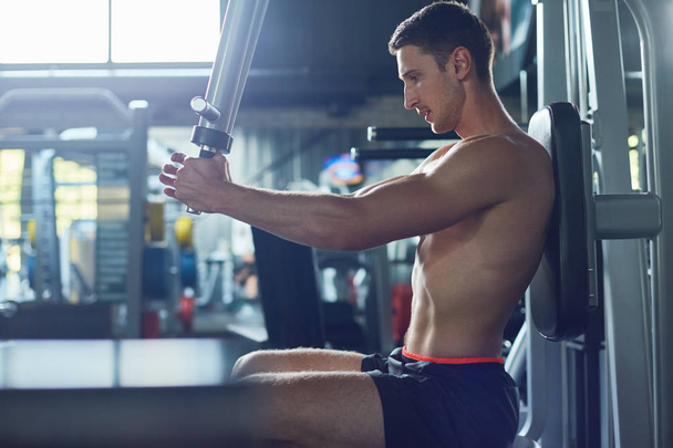 Vue du profil du sportif concentré entraînement haut du corps à l'aide d'une machine à peck deck, intérieur d'une salle de gym spacieuse en arrière-plan
 - Photo, image