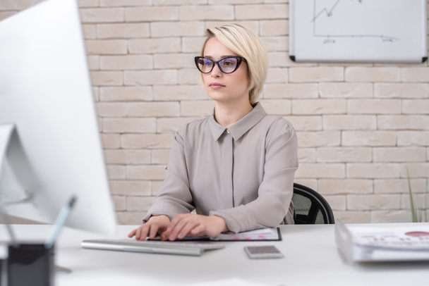 Портрет блондинки успішної бізнес-леді, використовуючи комп'ютер для роботи, сидячи за столом в сучасному офісі, аналізуючи дані
 - Фото, зображення