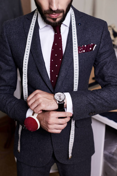 Retrato de seção intermediária de belo alfaiate barbudo vestindo terno elegante e jaqueta posando no estúdio atelier
 - Foto, Imagem