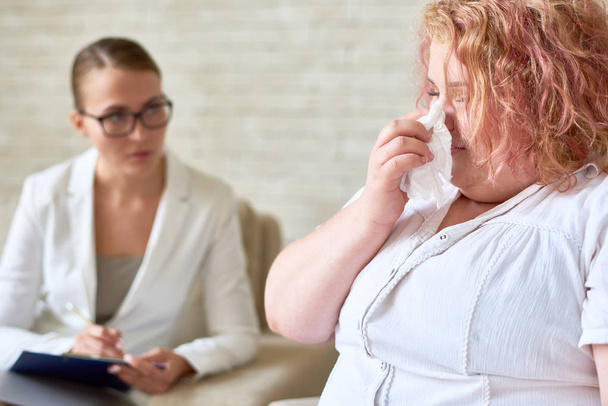 Portrait overweight woman crying wiping tears with tissue during therapy session with female psychiatrist - Φωτογραφία, εικόνα