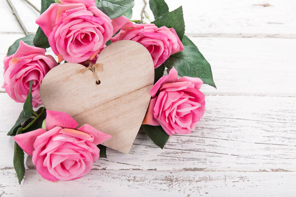 Flowers composition for Valentines, Mothers or Womens Day. Pink flowers with wooden hearth on old white wooden background. - Foto, imagen