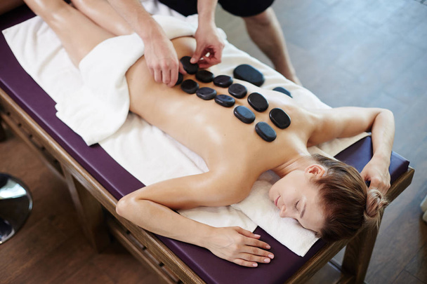 Portrait en angle élevé de jeune femme bénéficiant d'une thérapie de pierre allongée sur une table de massage au centre SPA
 - Photo, image