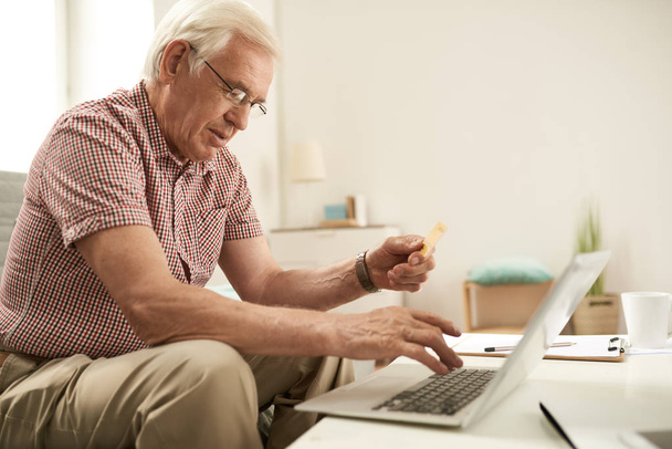 Seitenansicht Porträt eines älteren Mannes Online-Shopping per Laptop Eingabe von Kreditkartendaten für die Zahlung - Foto, Bild