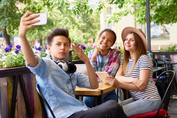 Groupe multi-ethnique de trois amis heureux prenant smartphone selfie dans un café en plein air. Asiatique homme tenant caméra
 - Photo, image