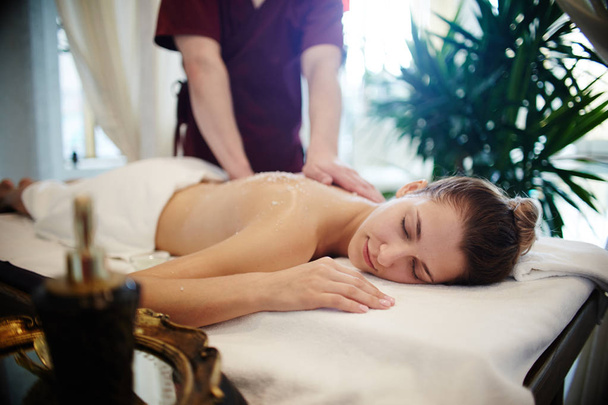 Portret van ontspannen jonge vrouw genieten van massage in het kuuroord, liggend op een massagetafel met ogen gesloten - Foto, afbeelding