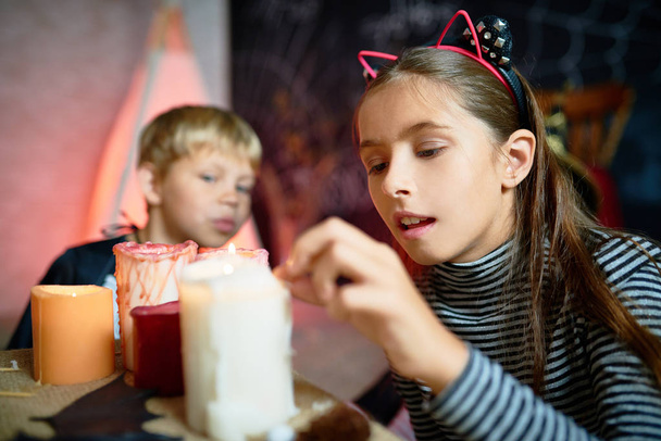 Retrato de niña bonita encendiendo velas en Halloween en la habitación decorada, niño pequeño con traje en el fondo
 - Foto, Imagen