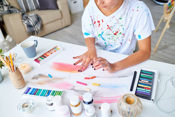 Retrato de alto ángulo de mujer joven creativa pintura de dedos cuadro con colores pastel en el escritorio en apartamento moderno
 - Foto, imagen