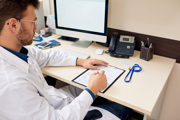 Ammattimaisen fyysikon muotokuva istuu toimistossa ja kirjoittaa työmuistiinpanoja potilaan muodossa, kopioi tilaa
 - Valokuva, kuva