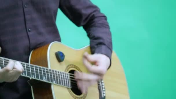 Close-up of a mans hands playing a guitar on green background - Materiał filmowy, wideo