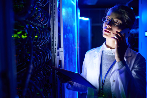 Retrato de una hermosa científica trabajando con supercomputadora en luz de neón, hablando por teléfono y sosteniendo una tableta digital
 - Foto, imagen