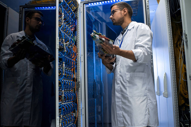 Nízký úhel portrét mladého muže na sobě plášť kontrolu blade servery při práci s superpočítač pro vědecké účely - Fotografie, Obrázek