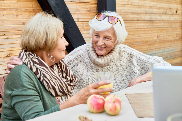 Cheerful senior women wearing knitted sweaters enjoying fresh air at lovely patio and chatting animatedly with each other - Фото, зображення