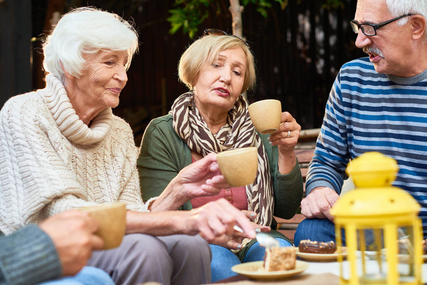 Ältere Menschen in warmer Kleidung genießen die Gesellschaft der anderen bei einer Teeparty mit leckerem Kuchen im Freien - Foto, Bild
